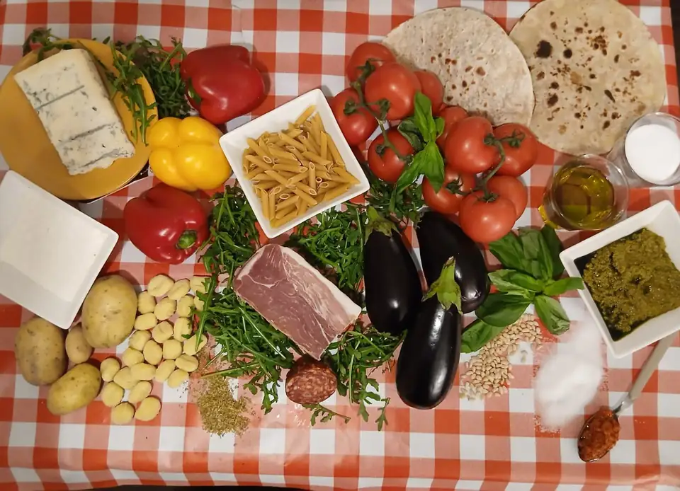 Zutaten von Cucina Massimo auf rot-weiss kariertem Tuch: Tomaten, Auberginen, Pesto, Rohschinken und Piadina-Fladen